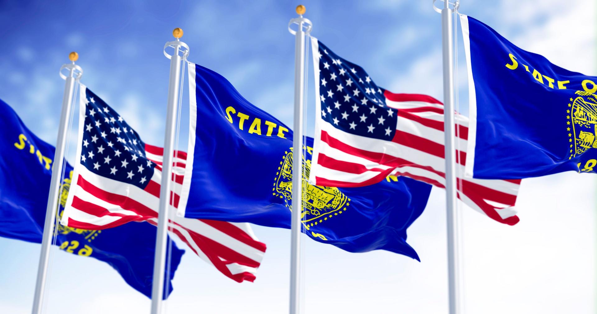 Oregon state flags waving in the wind with the american flags on a clear day